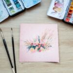 Aquarelle végétale représentant un bouquet de fleurs sur un papier teinté en rose en cours de réalisation par Christelle Lachambre artiste-peintre