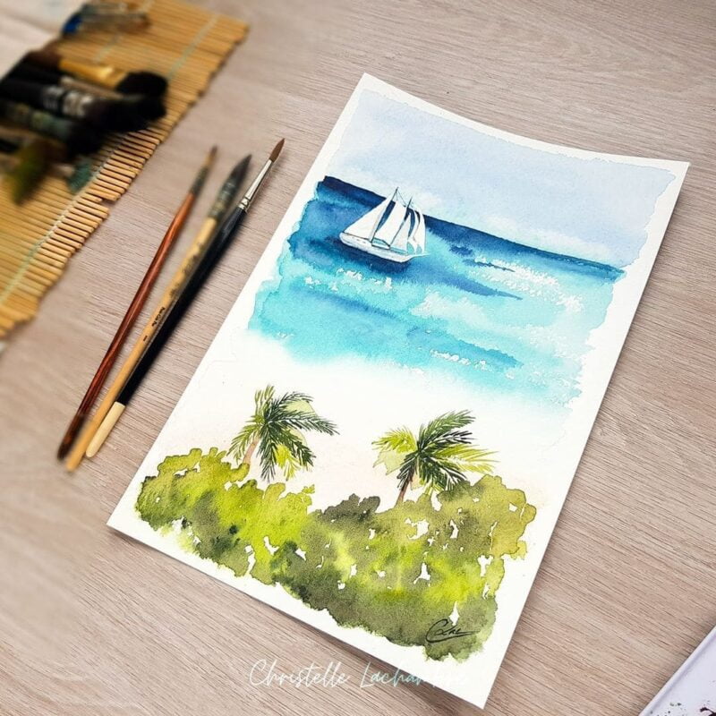 Aquarelle paysage représentant un voilier blanc sur une mer aux eaux turquoises devant une plage avec de la végétation en cours de réalisation par Christelle Lachambre artiste-peintre